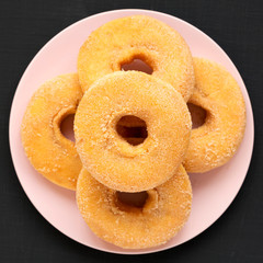 Homemade autumn apple-cinnamon donuts on a pink plate on a black background, view from above. Flat lay, overhead, top view.