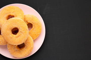 Top view, homemade autumn apple-cinnamon donuts on a pink plate on a black background. Flat lay, overhead, from above. Space for text.