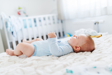 Side view of adorable caucasian six months old baby boy dressed in bodysuit lying in bed and looking up.
