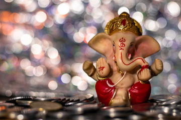Front shot of a Ganesha statue for Diwali decoration - natural lighting and a pile of coins in the foreground