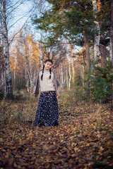 A pretty girl in a long skirt and sweater stands in the autumn forest.