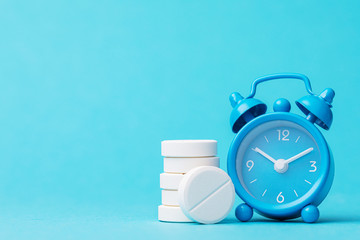 Pills and alarm clock on a blue background with copy space. Its time to take medicine