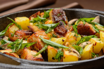 Fride potatoes with pieces of meat and herbs in a cast-iron pan. Closeup