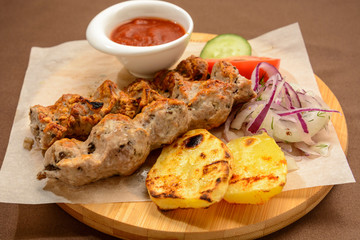 Kebab with fried potatoes, onion and vegetables on a wooden board.