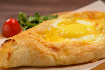Ajarian traditional khachapuri with egg. Tomato and greens in the background.