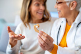 Modern hearing aids.The choice of hearing aid in the doctor's office. Doctor showing hearing aid. Otolaryngologist giving hearing aid to patient. The hearing aid for a senior woman