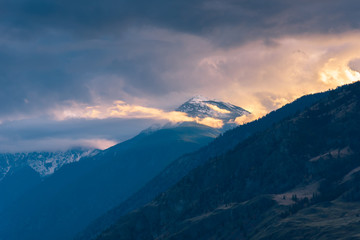 Obraz premium Snow-capped mountain glowing in sunset light with dramatic clouds and fog in Cawston, British Columbia, Canada
