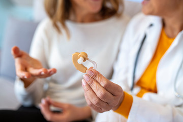 The doctor laryngologist explains senior woman how to wear a hearing aid. Mature female doctor hearing specialist in her office Showing Hearing Aid To female Patient In Clinic