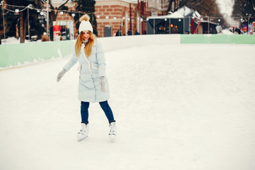 Girl in a winter park. Beautiful lady in a blue jacket. Woman in a ice arena