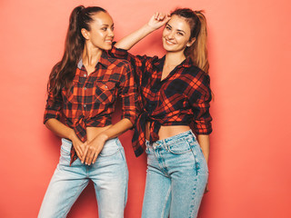 Two young beautiful smiling brunette hipster girls in trendy similar checkered shirt and jeans clothes.Sexy carefree women posing near blue wall in studio.Positive models having fun