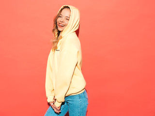 Portrait of young beautiful smiling girl in trendy summer hipster yellow hoodie.carefree woman posing near pink wall in studio. Positive model having fun