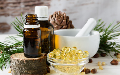 composition of cedar oil with pine nuts on a background of a branch with a pine cone, on a light wooden background