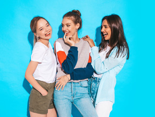 Three young beautiful smiling hipster girls in trendy summer clothes. Sexy carefree women posing near blue wall in studio. Positive models having fun and hugging