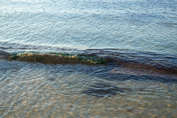 A long stone laying under the calm sea water near the beach