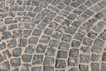 Cobbled road close-up. Pedestrian paving in street. Paved, detail. Brown texture of a paving stone track on sand.