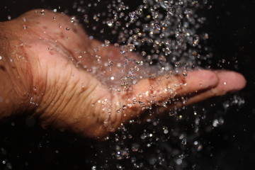 Fototapeta premium water falling on the man hand on the black background. man enjoying the water falling with his hand.