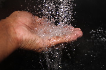 water falling on the man hand on the black background. man enjoying the water falling with his hand.