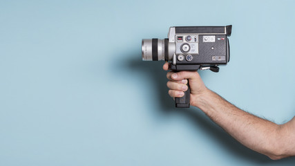 Close-up of man's hand holding old-fashioned camcorder against blue background