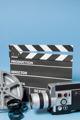 Clapperboard; camcorder camera; film reel and film stripes on blue backdrop