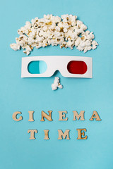 Anthropomorphic face made with popcorns and 3d glasses over the cinema time text against blue...