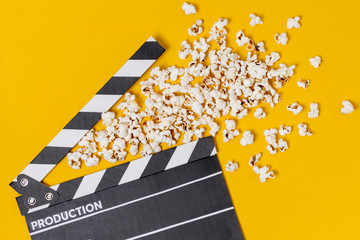 Movie clapperboard with popcorns on yellow background
