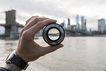 Hand holding a lens against New York City skyline - obrazy, fototapety, plakaty