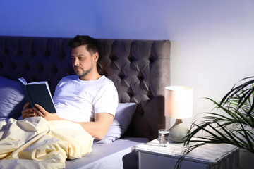 Handsome man reading book in dark room at night. Bedtime