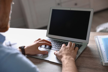 Man using laptop at table indoors, closeup. Space for text