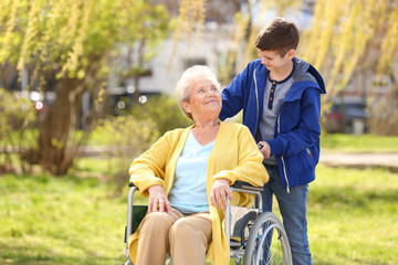 Senior woman in wheelchair with her grandson on sunny day outdoors