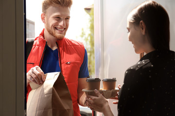 Courier giving order to young woman at open door. Food delivery service