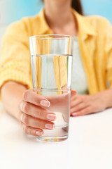 Woman holding glass of water at white table, closeup. Refreshing drink
