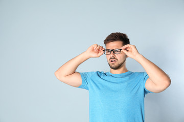 Young man with vision problems wearing glasses on grey background, space for text