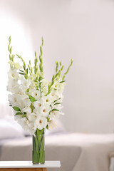 Vase with beautiful white gladiolus flowers on wooden table in bedroom