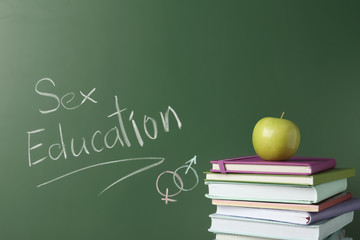 Books and apple near chalkboard with phrase 