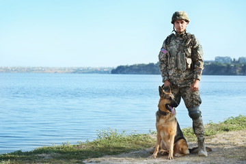 Man in military uniform with German shepherd dog near river, space for text