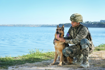 Man in military uniform with German shepherd dog near river, space for text
