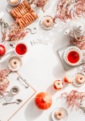 Autumn flat lay with word home, cozy tea setting, cakes , flowers, pumpkin and clipboard on white desktop background. Top view. Frame. Copy space for your text or design.
