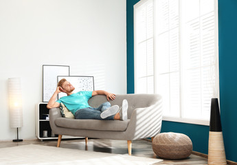 Happy young man resting on sofa under air conditioner at home