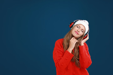 Young woman listening to music with headphones on dark blue background, space for text