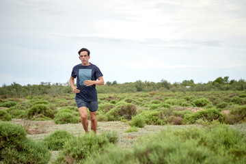 runner running in a field full of bushes, the boy is dressed in blue, and the field is green to the horizon