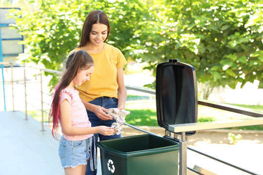 Mother and her daughter throwing paper into recycling bin outdoors