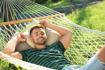 Young man resting in comfortable hammock at green garden