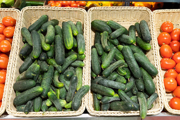 Green home-grown cucumbers and red ripe tomatoes in wicker baskets in supermarket