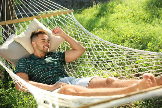 Young man resting in comfortable hammock at green garden