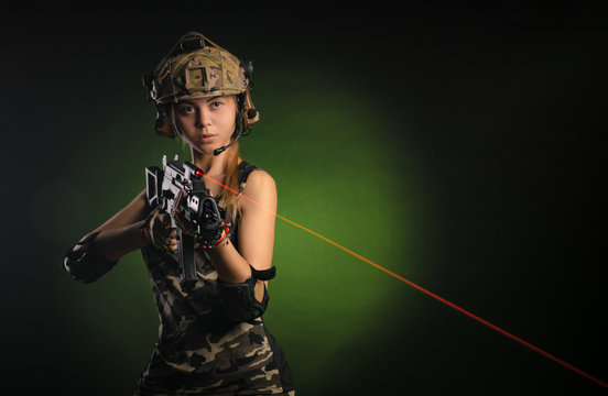 the girl in military airsoft clothes poses with a gun in her hands on a dark background