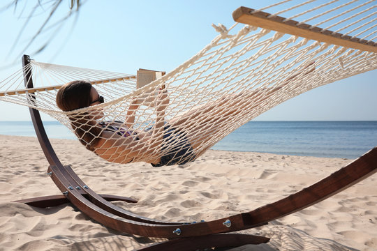 Young woman reading book in hammock on beach