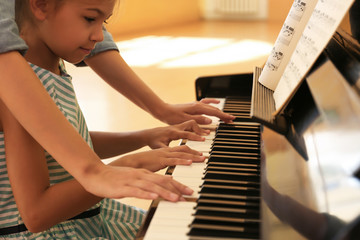 Young woman teaching little girl to play piano indoors