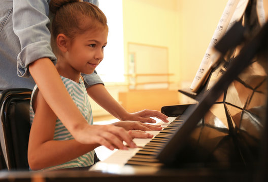 Young Woman Teaching Little Girl To Play Piano Indoors