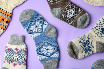 Different knitted socks on violet background, flat lay. Winter clothes