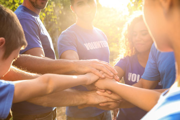 Group of volunteers joining hands together outdoors on sunny day